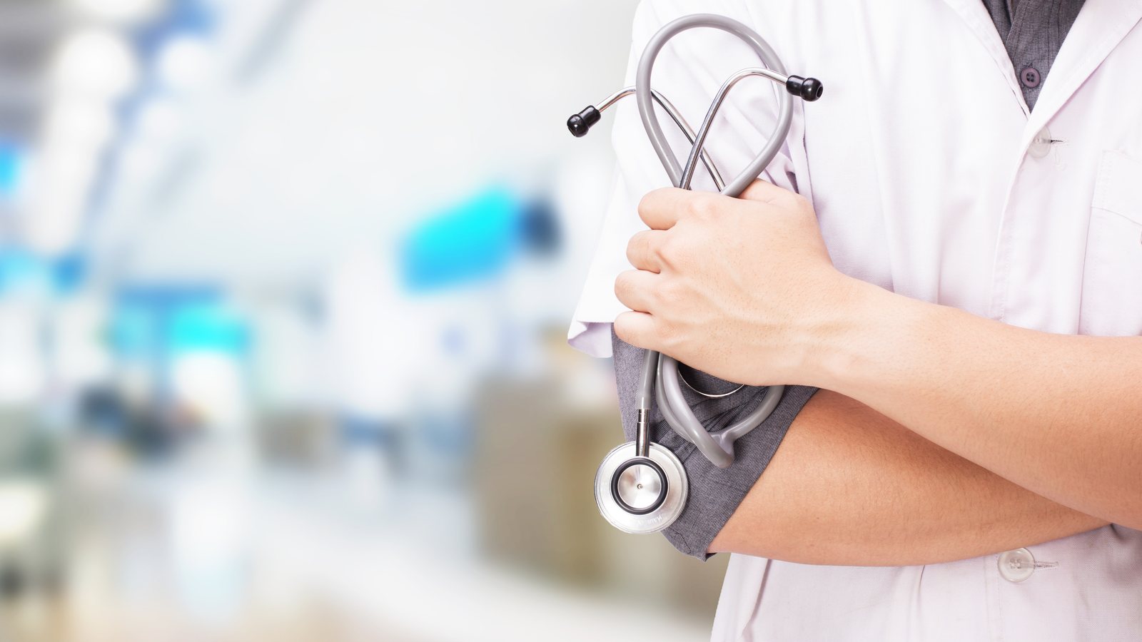 Médico de jaleco branco segurando estetoscópio em ambiente hospitalar